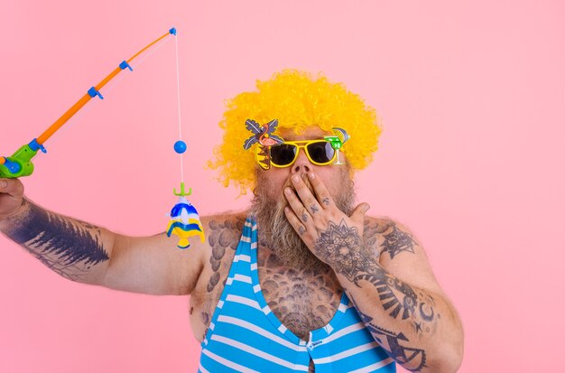 Hombre gordo asombrado con barba y gafas de sol divertirse con la caña de pescar