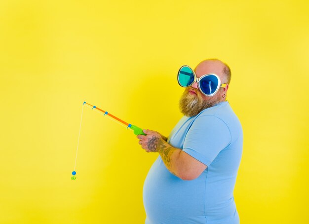 Hombre gordo con barba y gafas de sol no está contento con la caña de pescar