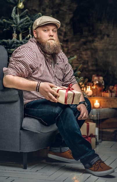 El hombre gordo y barbudo se sienta en una silla con un abeto de Navidad en el fondo.