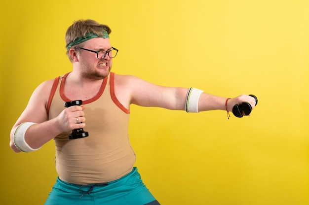 Hombre gordo con camisa negra haciendo ejercicio con pesas y mirando a cámara.