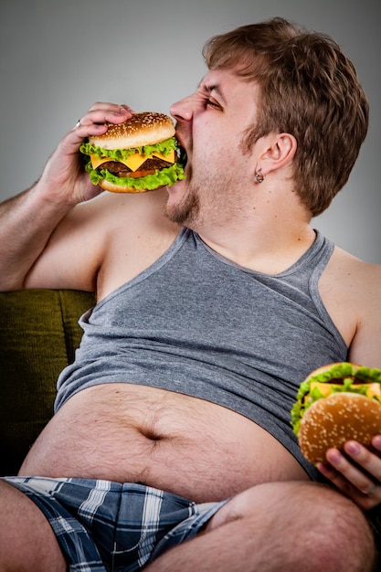 Hombre gordo comiendo hamburguesa sentado en un sillón