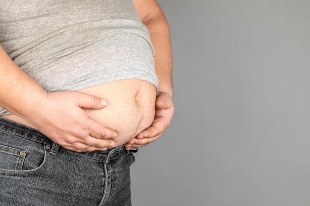 Foto hombre gordo comprobando su peso sobre un fondo gris