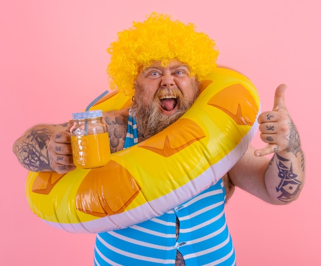 Hombre gordo feliz con peluca en la cabeza está listo para nadar con un salvavidas de rosquilla