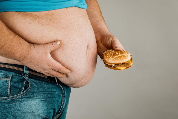 Hombre gordo con una hamburguesa en la mano sobre un fondo gris