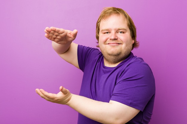 Hombre gordo pelirrojo auténtico joven sorprendido y sorprendido sosteniendo un espacio de copia entre las manos.