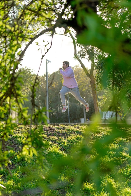 Hombre gordo en ropa deportiva saltando en el parque verde con la luz del sol desde atrás