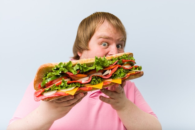 Hombre gordo rubio caucásico loco sosteniendo un sándwich gigante