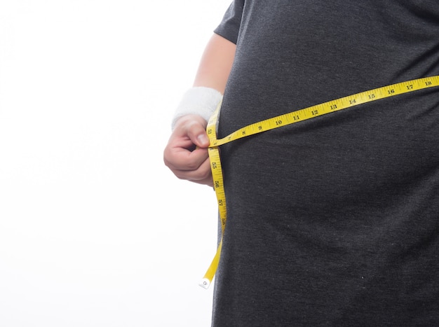 Hombre gordo sosteniendo una cinta métrica para ver su cuerpo aislado sobre fondo blanco.