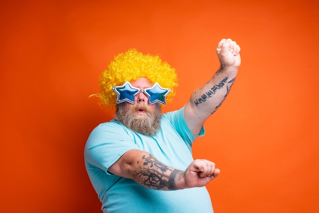 Foto hombre gordo con tatuajes de barba y gafas de sol baila música en una discoteca