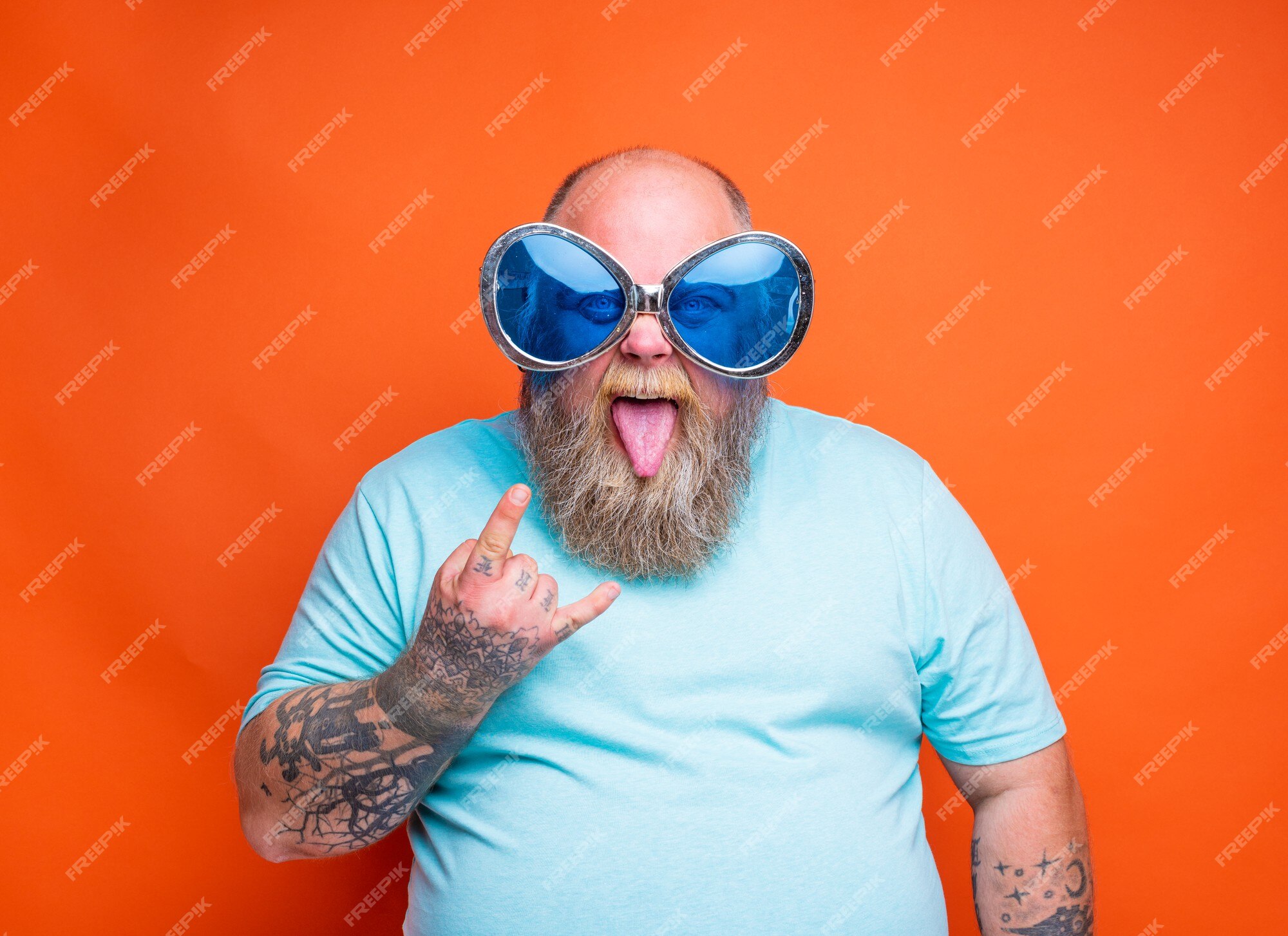 Hombre gordo con tatuajes de barba y gafas de sol hace el gesto de los | Foto Premium