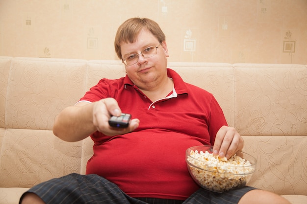 Hombre gordo viendo la televisión comiendo palomitas de maíz