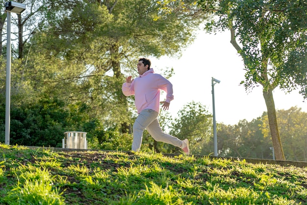 El hombre gordo viste ropa deportiva rosa y gris y hace deporte en el parque.