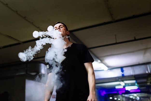 Hombre con gorra fuma un cigarrillo electrónico y libera nubes de vapor