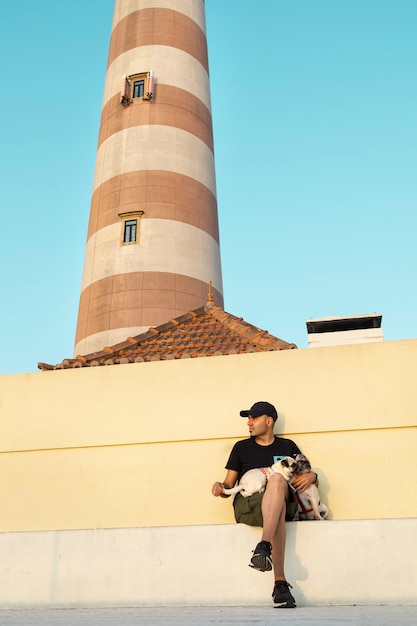 Hombre con gorra y gafas de sol con sus perros al atardecer junto al faro de Aveiro en Portugal