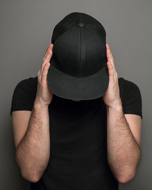 Hombre con gorra negra y camiseta contra un fondo gris