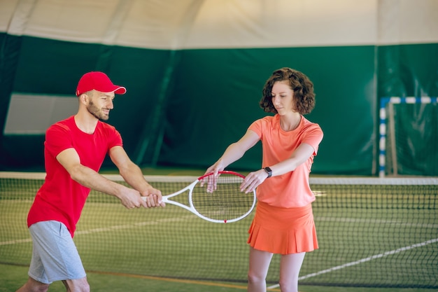 Hombre con una gorra roja y con una raqueta haciendo ejercicio con su entrenadora
