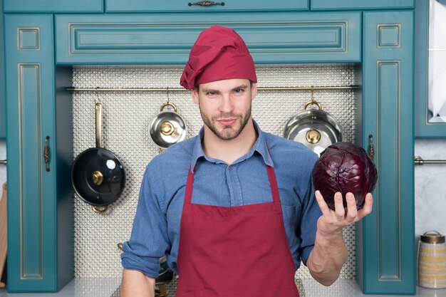 Hombre con gorro de cocinero, delantal con repollo morado en la cocina. Delicioso, delicioso, sabroso. Vegetariano, salud, concepto de dieta. Comida, cocción, preparación.