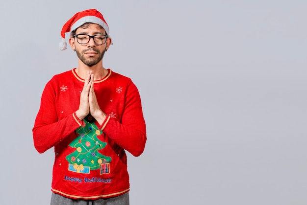 Hombre con gorro de navidad con las manos rezando aislado Chico con las manos juntas rezando en navidad aislado concepto de persona con gorro de navidad rezando y pidiendo un deseo