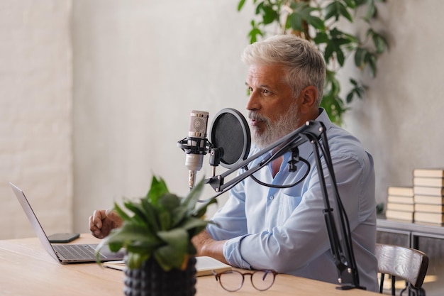 El hombre graba un podcast o una entrevista con un micrófono en un estudio de grabación, un adulto canoso