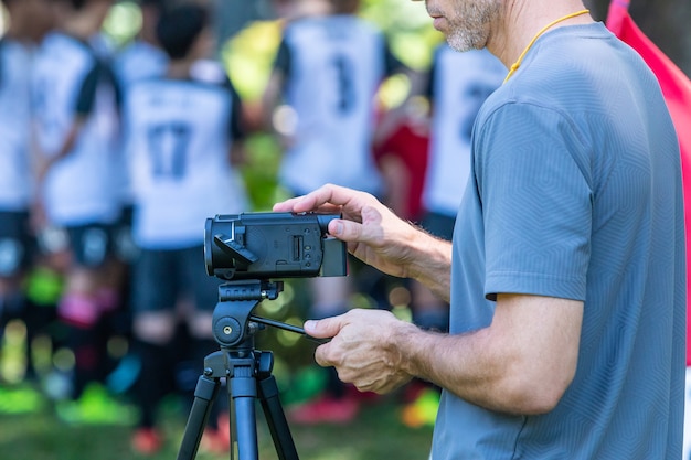 Foto hombre grabando un partido de fútbol con su cámara de video en un trípode en un campo al aire libre