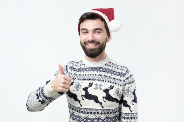 Hombre gracioso feliz con sombrero rojo de navidad muestra pulgares arriba y buena suerte