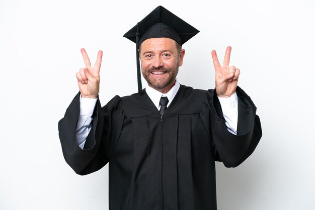 Hombre graduado universitario de mediana edad aislado de fondo blanco que muestra el signo de la victoria con ambas manos