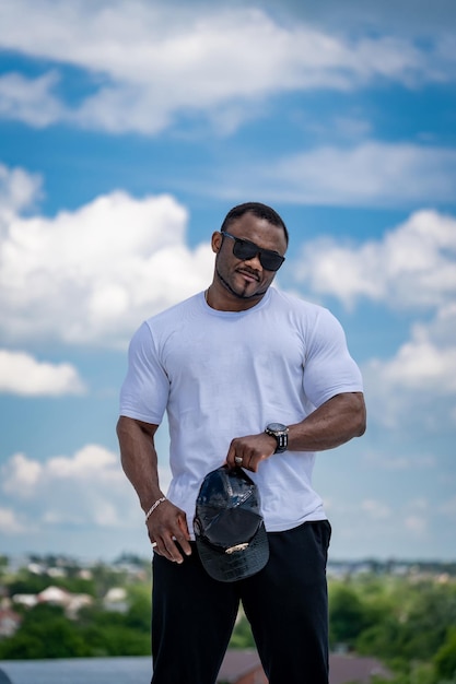 Hombre grande fuerte en gafas de sol al aire libre Hombre atlético guapo en camisa blanca de pie al aire libre