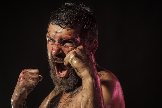 El hombre grita en posición de pelea con sangre en los puños de la cara