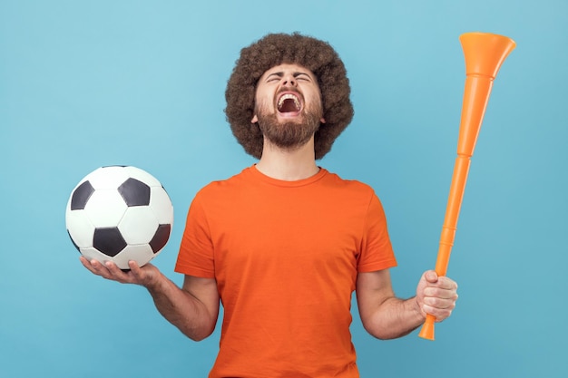 Hombre gritando celebrando la victoria del equipo de fútbol favorito sosteniendo cuerno y pelota