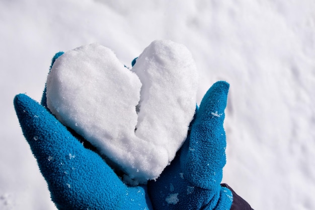 Un hombre con guantes azules sostiene la nieve en sus brazos en forma de corazón Se divide en dos partes Símbolo de separación y ruptura