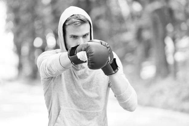 Hombre con guantes de boxeo y capucha en el paisaje natural Ejercicio de boxeador al aire libre Knowckout Hombre golpeando Lucha por el éxito Entrenando sus habilidades de boxeo Nacido para luchar Poder y energía