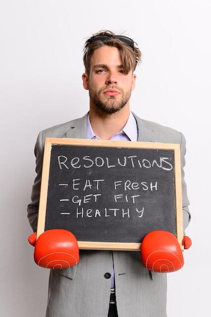 Hombre con guantes de boxeo rojos sobre fondo blanco. El hombre de negocios sostiene una pizarra con un cartel que señala resoluciones de estilo de vida saludable. Boxeador en traje formal con rostro serio. Concepto de salud y fitness