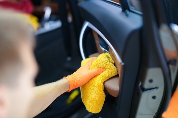 Foto hombre con guantes de goma limpiando el polvo de la puerta del coche con un paño de microfibra closeup