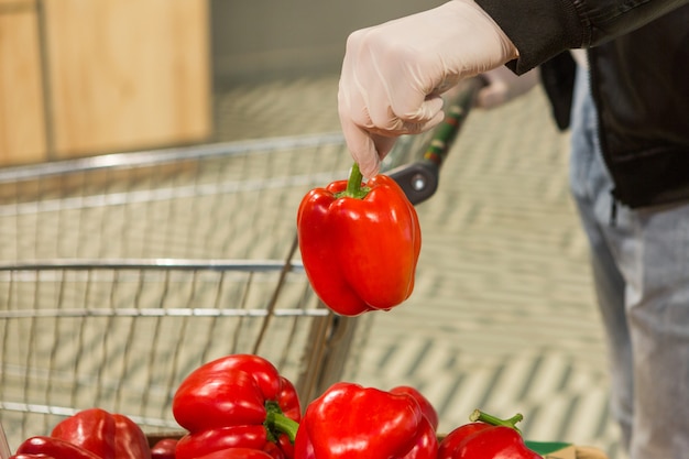 Hombre en guantes de látex blanco elegir pimiento rojo en la tienda. precauciones durante la cuarentena