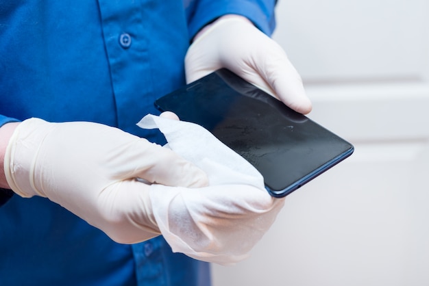 Hombre con guantes de látex desinfecta el teléfono con toallitas de limpieza