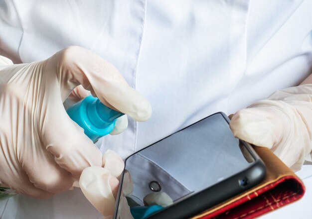 Hombre con guantes de látex que limpia el teléfono inteligente con alcohol desinfectante para manos y limpie con un paño. Limpiar su teléfono móvil de virus y gérmenes.