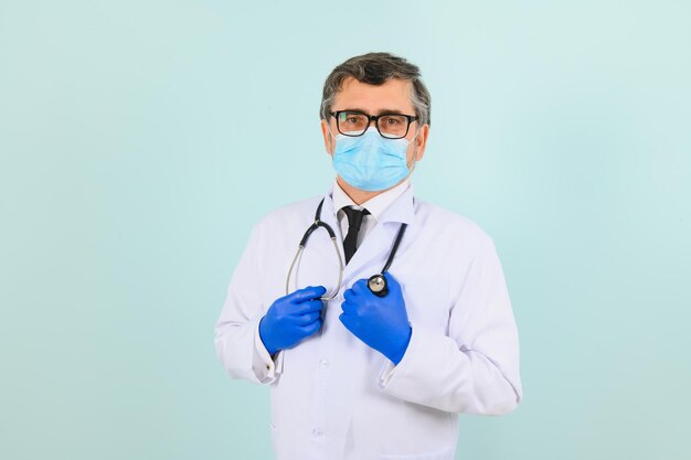 Hombre con guantes médicos poniéndose una máscara protectora contra el fondo azul.