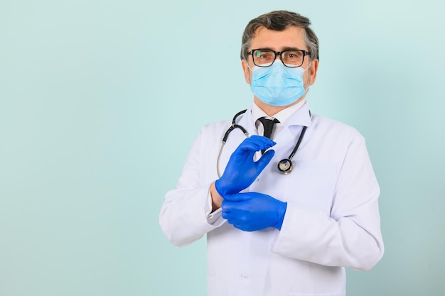 Hombre con guantes médicos poniéndose una máscara protectora contra el fondo azul.