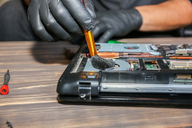 El hombre con guantes negros está reparando una computadora portátil. Trabajador del centro de servicio limpiando el polvo.