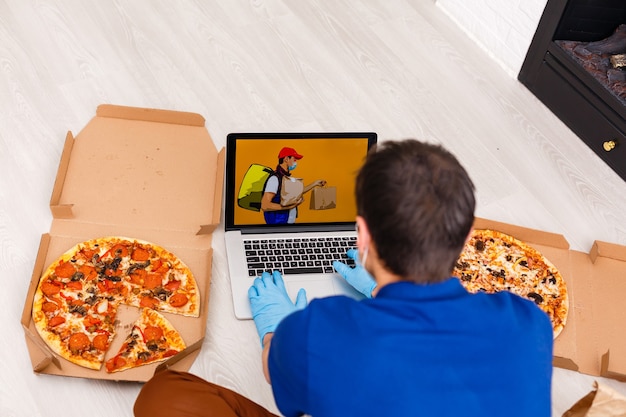 Hombre con guantes protectores y máscara con laptop para pedidos de alimentos en línea durante la cuarentena, primer plano. Servicio de entrega