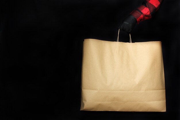 Un hombre con guantes protectores negros sostiene una bolsa de papel con compras en la tienda durante las vacaciones del Viernes Negro.