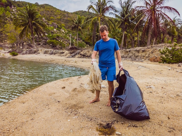 Hombre con guantes recoge bolsas de plástico que contaminan el mar Problema de basura basura basura derramada en la arena de la playa causada por la contaminación artificial y la campaña ambiental para limpiar el concepto de voluntario