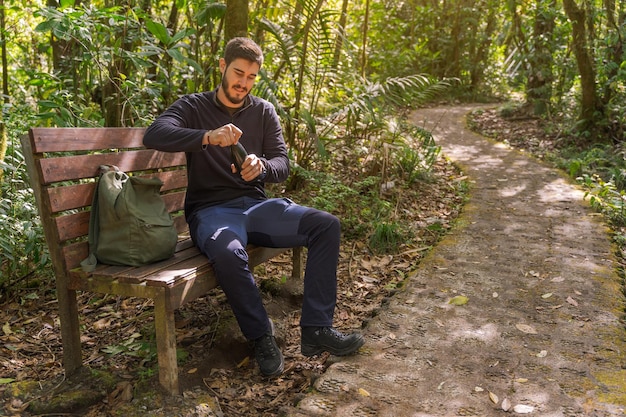 Hombre guapo abriendo botella en el bosque