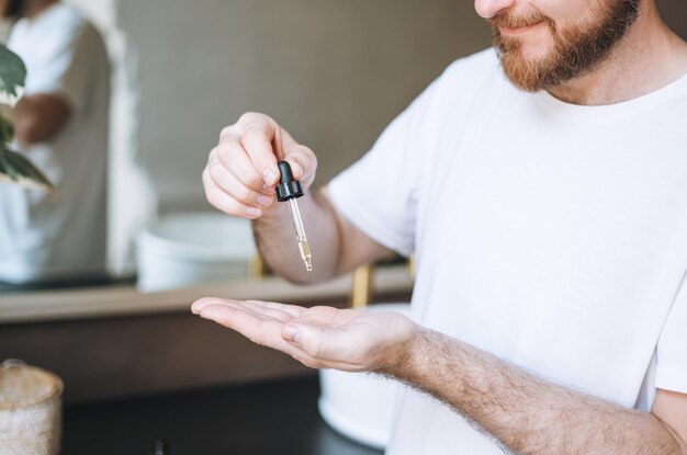 Hombre guapo adulto con pipeta con aceite de barba en el baño en casa