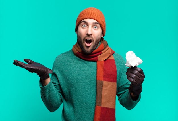 Hombre guapo adulto que parece sorprendido y conmocionado, con la mandíbula caída sosteniendo un objeto con una mano abierta en el costado. enfermedad y concepto de resfriado