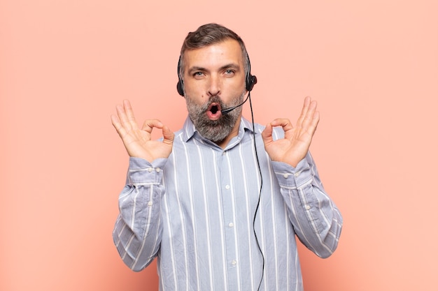 Hombre guapo adulto que se siente conmocionado, asombrado y sorprendido, mostrando aprobación haciendo un signo bien con ambas manos