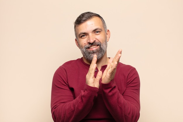 Hombre guapo adulto que se siente feliz y exitoso, sonriendo y aplaudiendo, diciendo felicitaciones con un aplauso