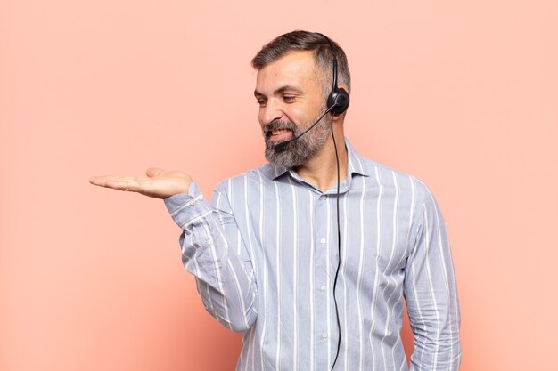 Hombre guapo adulto que se siente feliz y sonriendo casualmente, mirando a un objeto o concepto sostenido en la mano del lado