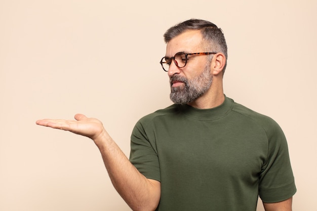 Hombre guapo adulto que se siente feliz y sonriendo casualmente, mirando a un objeto o concepto sostenido en la mano del lado