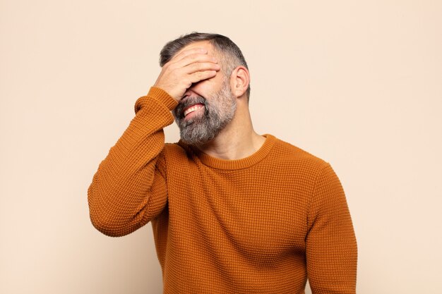 Hombre guapo adulto riendo y golpeando la frente como diciendo ¡oh! Lo olvidé o fue un error estúpido
